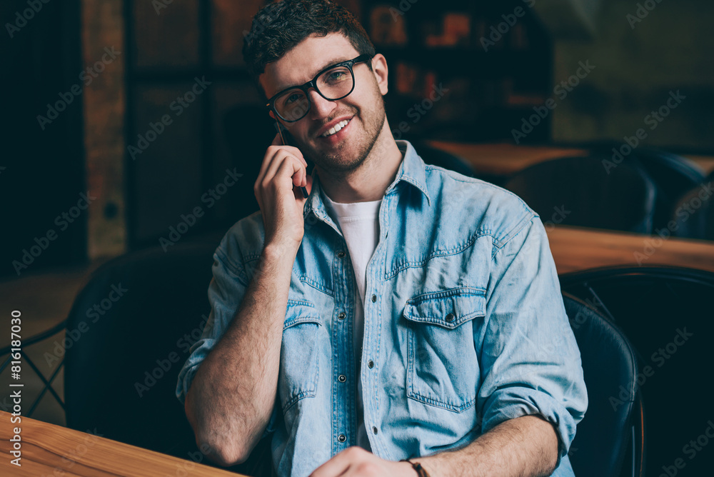 Poster portrait of happy cheerful hipster guy looking at camera and consulting with colleague vie telephone