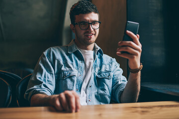 Happy cheerful hipster guy watching funny comedy show via mobile application connected to wireless...