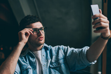 Handsome hipster guy in spectacles for vision correction making selfie photos for attracting...