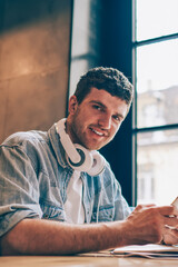 Portrait of cheerful smiling hipster guy with electronic headphones on neck looking at camera while...