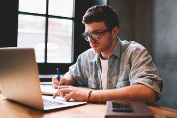 Concept of technology and communication, clever male copywriter in eyeglasses keyboarding on laptop...