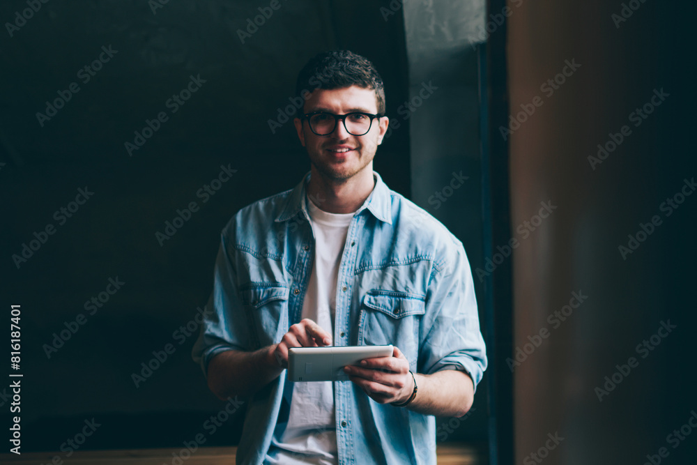 Poster portrait of cheerful hipster guy with cute smile on face using digital tablet for searching language