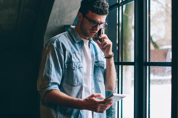 Serious hipster guy checking account balance during telephone call while making payment online on...