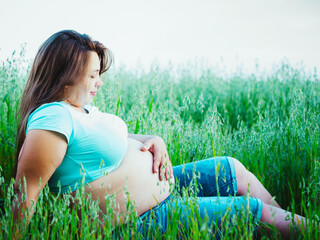 Beautiful pregnant woman sitting outdoors. Pretty pregnant woman looking at her belly and holds his...
