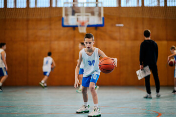 A junior basketball player is action, dribbling a ball on court.