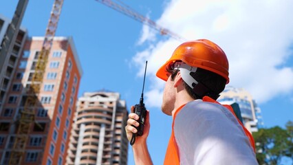 Male construction worker with walkie-talkie at construction site standing outdoors. Business,...