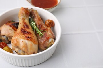 Marinade, roasted chicken drumsticks, rosemary and tomatoes on white tiled table, closeup. Space for text