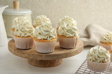 Tasty vanilla cupcakes with cream on white wooden table