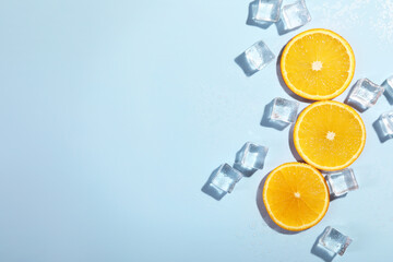 Slices of juicy orange and ice cubes on light blue background, flat lay. Space for text