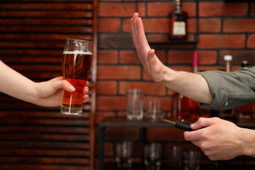 Man with car keys refusing from alcohol while woman suggesting him beer in bar, closeup. Don't drink and drive concept