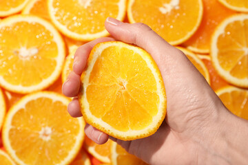 Woman squeezing juicy orange near slices of fruit, top view
