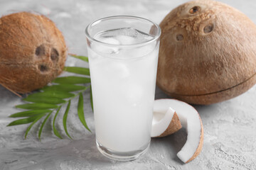 Glass of coconut water with ice cubes, palm leaf and nuts on grey table