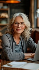 A woman in glasses is sitting at a desk with a laptop and a cup of coffee. She is focused on her work, possibly typing or browsing the internet. Concept of productivity and concentration