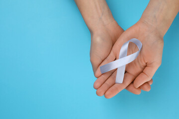 International Psoriasis Day. Woman with light blue ribbon as symbol of support on light blue background, top view. Space for text