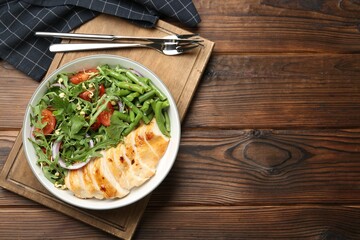 Healthy meal. Tasty salad and chicken breast in bowl and cutlery on wooden table, top view. Space for text
