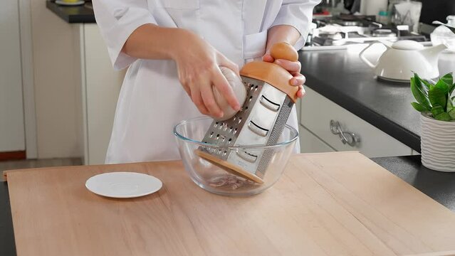The chef grates the ham into a glass bowl using a large grater. Ham filling for puff pastry. Appetizers with ham. Close-up, macro, front view