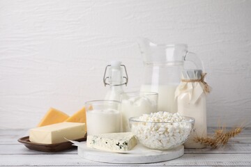 Different fresh dairy products and wheat ears on white wooden table