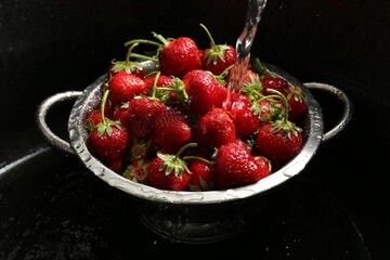 Washing fresh strawberries under tap water in metal colander in sink