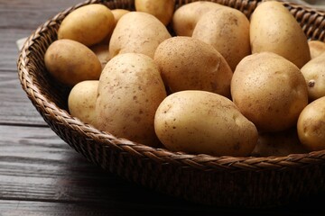 Raw fresh potatoes in wicker basket on wooden table, closeup