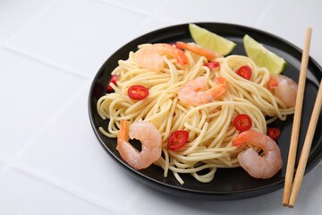 Tasty spaghetti with shrimps, chili pepper and lime on light tiled table, closeup. Space for text