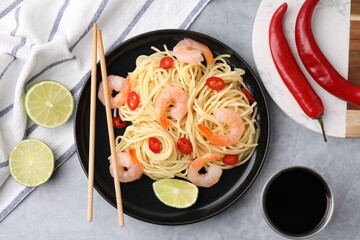 Tasty spaghetti with shrimps, chili pepper, lime and soy sauce on grey table, flat lay