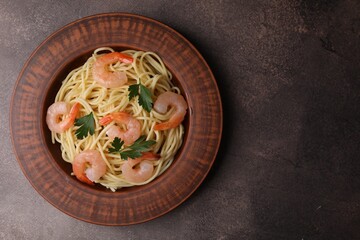 Tasty spaghetti with shrimps and parsley on brown textured table, top view. Space for text