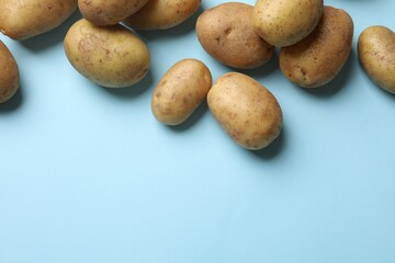 Many fresh potatoes on light blue background, flat lay. Space for text