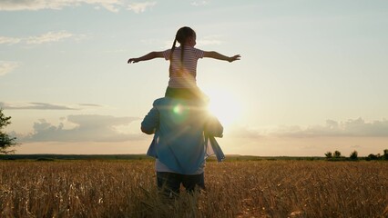 Little daughter on shoulders of her father. Girl and dad are traveling through wheat field. Child...