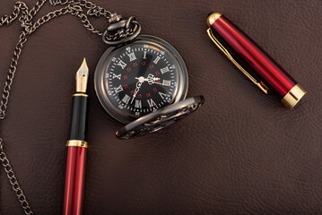 Fountain pen and antique pocket watch on leather surface, selective focus