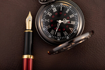 Fountain pen and antique pocket watch on leather surface, selective focus