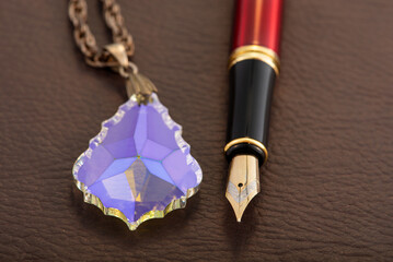 Fountain pen and crystal positioned on brown leather surface, selective focus