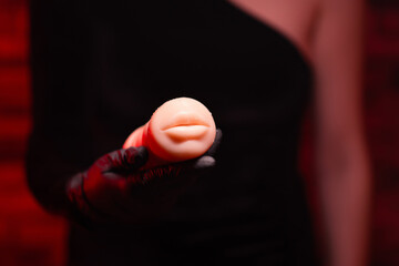 Sex toys for men. An artificial mouth-shaped masturbator made of silicone in the hands of a girl in black gloves and a black dress on a red background. Sex shop Adult store