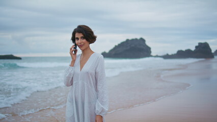 Outdoors girl talking mobile at rocky beach. Closeup smiling lady looking camera