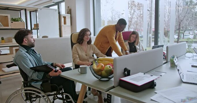 A modern office scene with a diverse group of employees, including a man in a wheelchair, engaging in a collaborative brainstorming session.