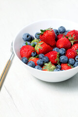 White bowl with fresh seasonal strawberries and blueberries
