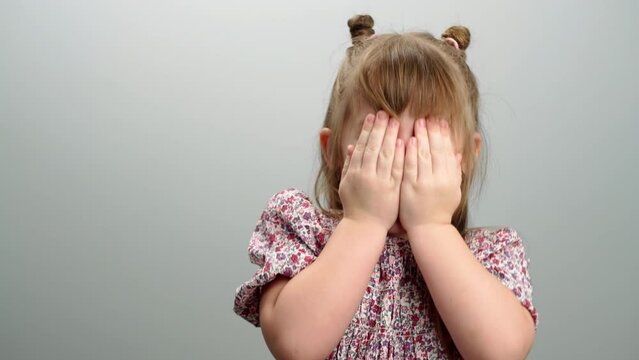 Background video of children's emotions, a portrait of a girl covering her face and smiling. The child is playing hide and seek, a happy childhood. High quality 4k footage