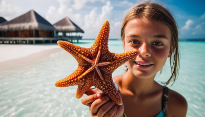 A tourist girl in close up on a sandy beach of the Maldives in the water holds a starfish in her hands. An interesting photo of a trip to a tropical country.
