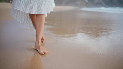 Woman legs leaving footprints at ocean shore closeup. Carefree girl walking sand