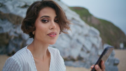 Pretty lady using smartphone at seashore closeup. Relaxed woman looking camera