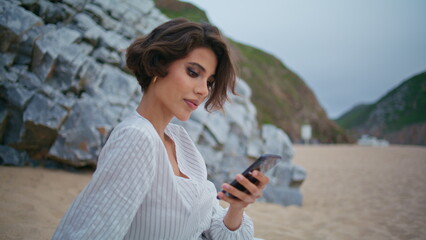 Relaxed girl browsing smartphone on sandy shore closeup. Attractive lady rest 
