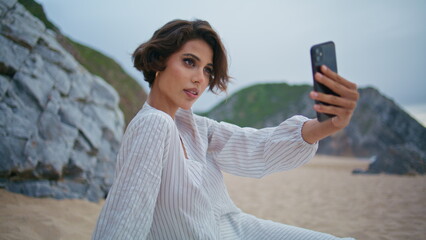 Beautiful blogger taking smartphone pictures on sandy beach outdoors closeup.