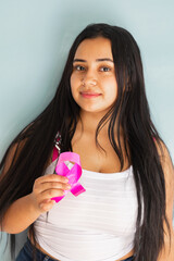 Brunette Latin woman holding a pink ribbon on a green background