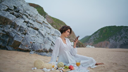 Carefree woman checking mobile phone on beach. Relaxed girl rest picnic at shore