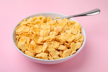 Breakfast cereal. Tasty corn flakes in bowl and spoon on pink table, closeup