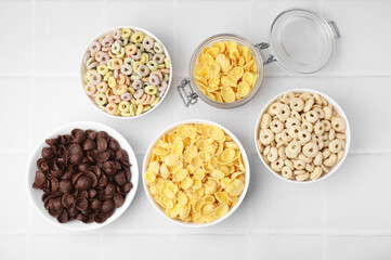 Different delicious breakfast cereals on white tiled table, flat lay