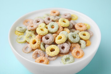 Tasty colorful cereal rings and milk in bowl on turquoise background, closeup