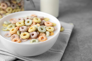 Tasty colorful cereal rings and milk in bowl on grey table, closeup. Space for text