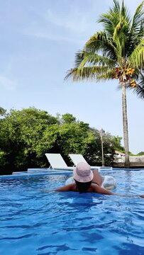 Young woman relaxing inside swimming pool at hotel during summer holiday vacations.