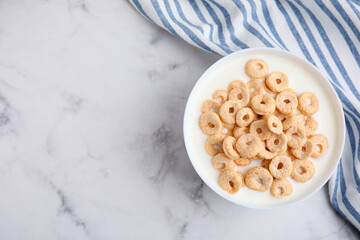 Breakfast cereal. Tasty corn rings with milk in bowl on white marble table, top view. Space for text