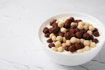 Breakfast cereal. Tasty corn balls with milk in bowl on white textured table, closeup. Space for text